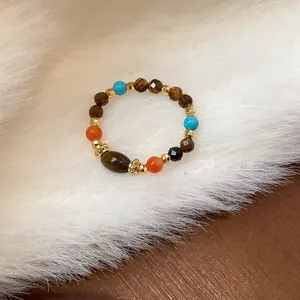 Dettaglio di un anello elastico con perline in occhio di tigre, turchese e corniola.