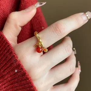 Primo piano che mostra il dettaglio dell'anello di bambù dorato con ciondolo rosso.