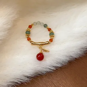Dettaglio di un anello elastico di perline con ciondolo a bambù dorato e pietre naturali.