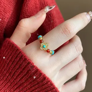 Dettaglio macro di un anello elastico con perline turchesi e ciondolo a fiore dorato