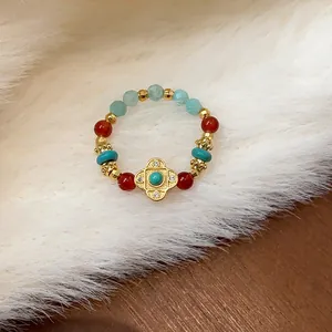 Dettaglio macro di un anello elastico con perline colorate e ciondolo a trifoglio dorato