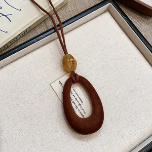Primo piano di una collana con ciondolo ovale floccato marrone e dettaglio in resina dorata.
