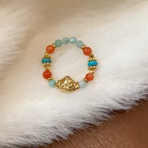 Dettaglio di un anello elastico con perline colorate e un pendente testa di volpe dorato.