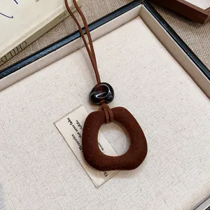 Dettaglio del ciondolo geometrico floccato marrone e della perla in resina liscia sulla collana