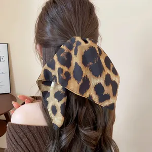 Elegante elastico per capelli con fiocco leopardato su lunghi capelli castani mossi da dietro.