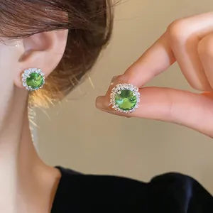 Detail of emerald green square stud earrings with a sparkling diamond-like halo design.