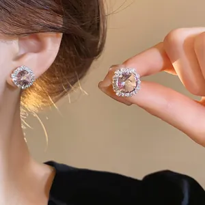Close-up of elegant pink crystal halo stud earrings worn on ear and held by fingers.
