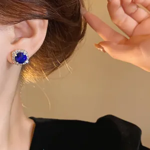 Detailed close-up of a blue gemstone earring with a sparkling crystal halo on a model.
