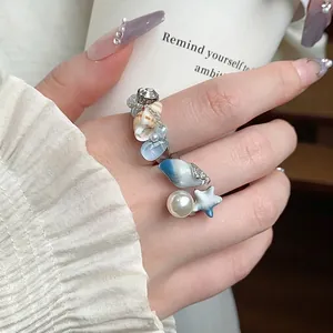 Elegante anello a tema oceanico con perle e conchiglie su una mano che tiene una tazza