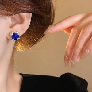 Close-up of royal blue crystal halo stud earrings worn on ear with elegant jewelry vibe
