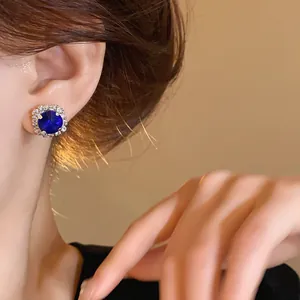 Close-up of an elegant blue gemstone stud earring worn on the ear with a crystal halo