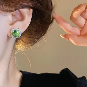Macro view of an elegant emerald green halo stud earring with sparkling stones on ear