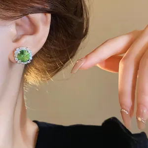 Close-up of elegant emerald green stud earring with shimmering crystal halo on ear