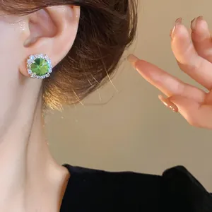 Close-up of elegant halo stud earrings with round green emerald-style crystal on model