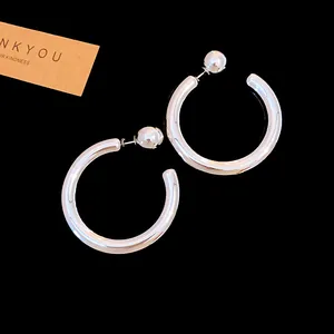 Close-up of minimalist silver metallic C-shaped hoop earrings with glossy ball stud backings