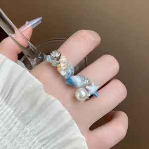 Dettaglio ravvicinato dell'anello aperto con conchiglia e perla indossato al dito