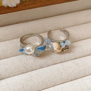Dettagli macro di un anello con perla e smalto blu e un anello aperto con conchiglia naturale