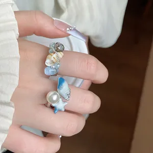 Primo piano di anelli regolabili con elementi di conchiglie, perle e stelle marine.