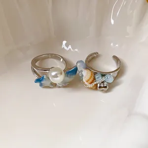 Vista dettagliata di due eleganti anelli argentati a tema marino con perle e conchiglie.