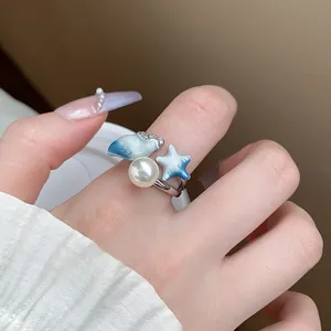 Dettaglio di anello con perla e ciondoli a conchiglia e stella in smalto blu