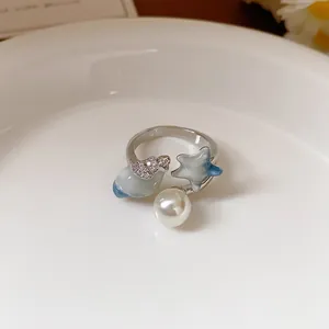 Dettaglio di un anello aperto con perla, stella marina blu e conchiglia zircone