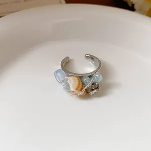 Vista macro di un elegante anello a conchiglia con perline blu e dettagli in cristallo