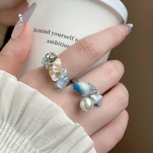 Dettaglio ravvicinato di un anello aperto di moda con perle e ciondoli a forma di conchiglia.