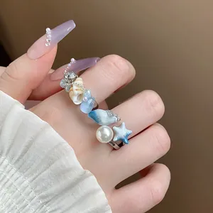 Dettaglio di un anello a tema oceano con perla, conchiglia e ciondoli a stella marina