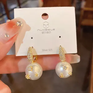 Detail view of gold-plated pearl drop earrings with star-shaped cubic zirconia studs