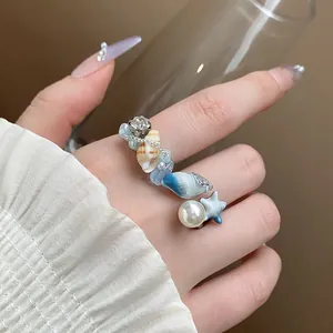 Primo piano di un anello aperto a tema oceano con perle finte e ciondoli a conchiglia.