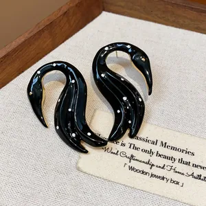 Primer plano de pendientes de cisne en esmalte negro con lunares blancos y oro