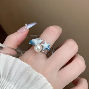Vista dettagliata di un anello aperto chic con perla, conchiglia blu e design a forma di stella marina