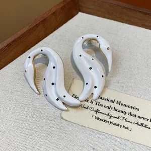 Primer plano de pendientes de cisne en esmalte blanco con lunares y borde dorado