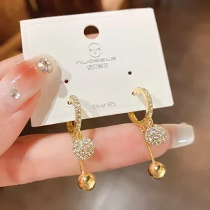 Detail of gold-plated hoop earrings with crystal-studded ball and gold sphere drop