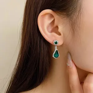 Elegant silver-toned earrings with green teardrop stones displayed on a model's ear