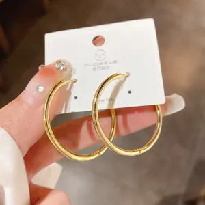 Close-up detail of large minimalist gold-plated hoop earrings on white jewelry display card