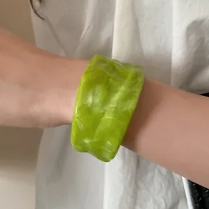 Close-up detail of a vibrant lime green marbled resin cuff bracelet with wavy edges.