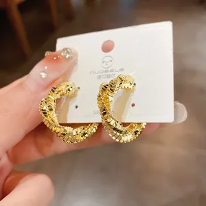 Detailed close-up of elegant gold-plated twisted hoop earrings with fine scale texture
