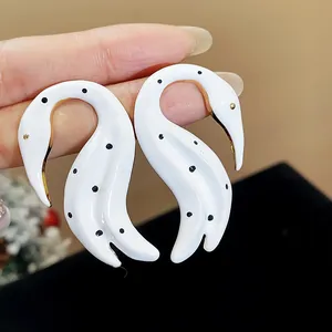 Primer plano detallado de elegantes pendientes de cisne en esmalte blanco con lunares negros