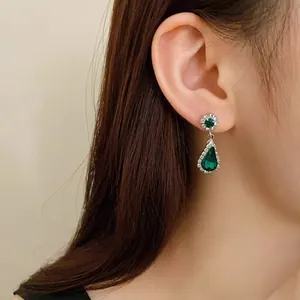 Elegant close-up of a green teardrop dangling earring worn by a female Asian model
