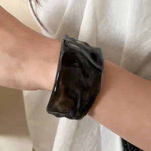 Close-up of a smoky black translucent rippled cuff bracelet on a female wrist.