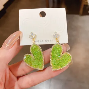 Close-up detail of vibrant green heart-shaped earrings with gold plating and zircons