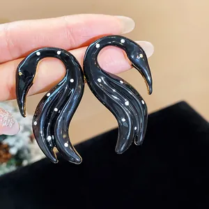 Primer plano de elegantes pendientes de cisne en esmalte negro con lunares blancos y plata.