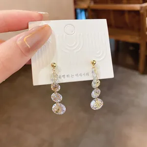 Close-up of gold-plated dangling earrings with zircon stones and flower patterns on white card