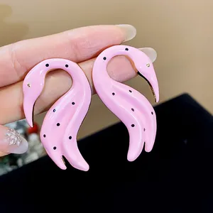 Primer plano detallado de pendientes de cisne en esmalte rosa con lunares negros y oro