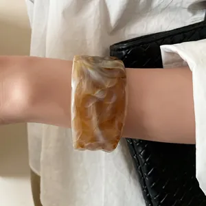Detail shot of elegant amber marbled wide resin cuff bracelet worn on a woman's wrist