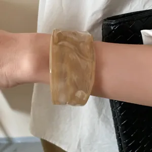 Detailed close-up showing a wide marbled resin bangle with beige and cream wavy patterns on a wrist