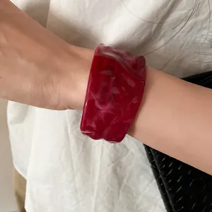 Close-up detail of a marbled red resin cuff bracelet with textured pleated design