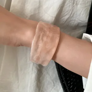 Detailed view of a stylish wide marbled peach resin bangle worn on a model's wrist