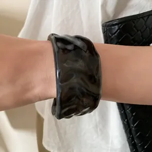 Close-up of wide tortoiseshell acrylic bangle with rippled texture worn on wrist
